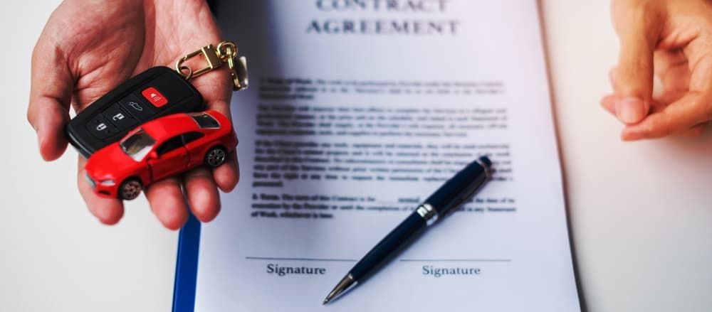 Business hand holds red car toy, keyless, pen, contract buy/sell, insurance and settlement agreements.