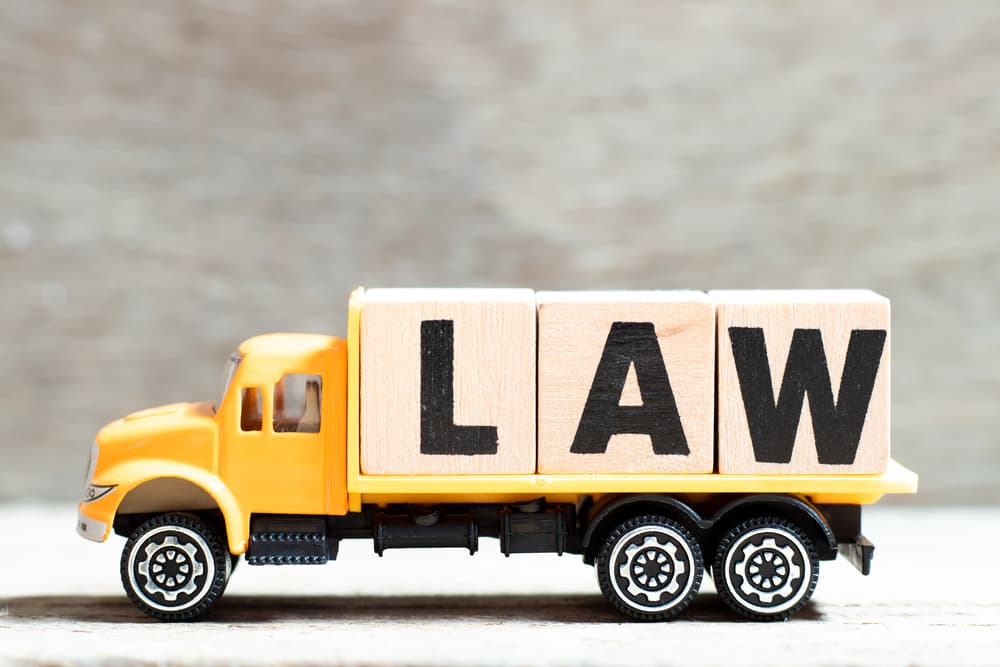 A truck clutching letter blocks spelling "law" against a wooden backdrop.